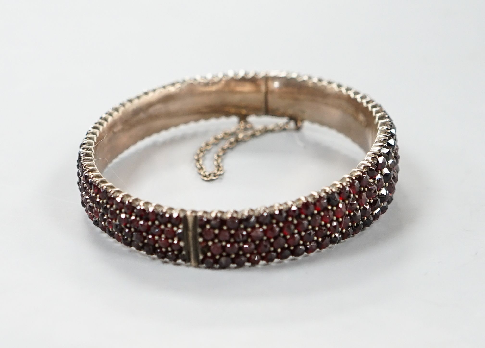 A late Victorian gilt white metal and garnet encrusted hinged bangle (stone missing).